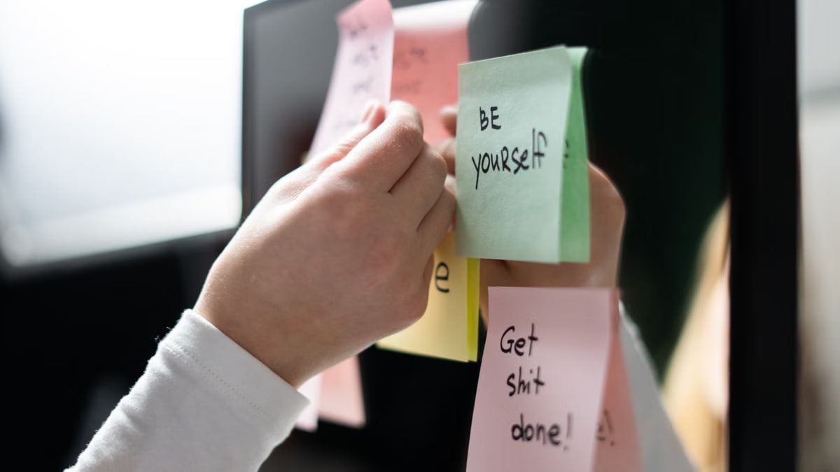 Close-up of hand placing colorful motivational sticky notes on a mirror, inspiring messages.